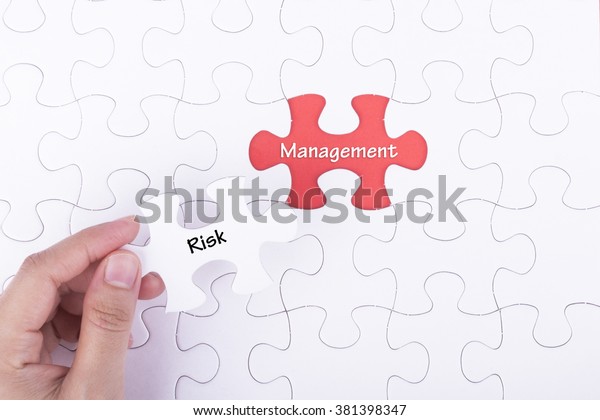 Hand\
embed missing a piece of puzzle into place, red space with word\
RISK MANAGEMENT. Business and financial\
concept.