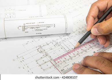Hand engineer holding a pencil, writing on the blueprint of construction industry . Place the rolls on a desk over blurred blueprint for construction industry background. construction industry concept