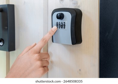 Hand Entering Code on Wall-Mounted Lockbox. Close-up of a person entering a numeric code on a combination key lockbox mounted to a wooden wall for secure access.