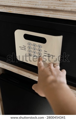 Hand entering security code on hotel room safe keypad to lock valuables inside wooden closet
