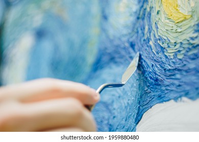 the hand of a European artist holds a mastekhin smeared in oil paint and draws a picture. Van Gogh's replica Starry night. blurred background. Close-up.
