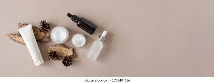 Hand, Eye, Facial Moisturizer Cream, Serum, Essential In Glass Bottles And Pine Bark And Cone On Beige Background Flat Lay, Top View. Set For Skin And Body Care Beauty Products Banner Format