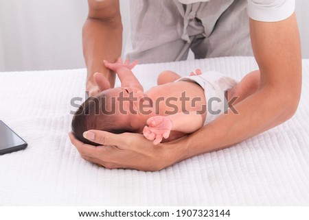 Hand of father hold his first child newborn with strong arm carefully on white bed, multitask fatherhood help mother feeding baby son by stop business talk putting the smartphone on bed