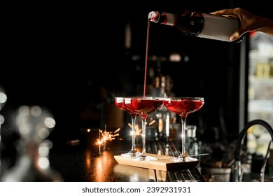 Hand of female bartender holds bottle of berry syrup and pours it in thin stream into martini glasses. Woman making fresh cocktails at bar - Powered by Shutterstock