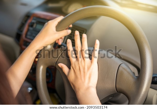 Hand female on the steering wheel of a\
car while driving the windshield and road. Close up of woman hand\
presses the horn on the steering wheel on her\
car.