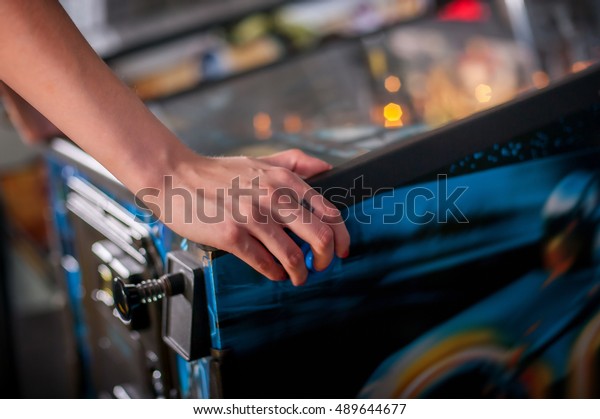 Hand of female pressing button and playing\
pinball machine