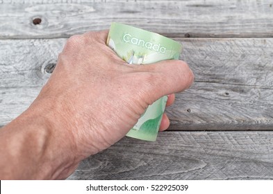 Hand fiercefully  holding a roll full of green bank notes against a wooden background