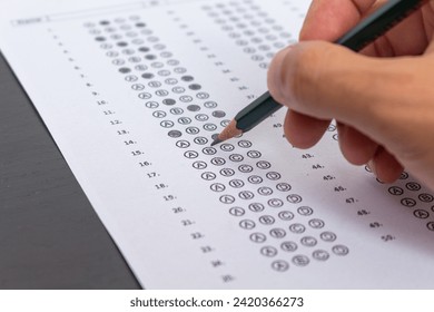 Hand filling out an exam answer sheet with a pencil, concept for public and entrance exams.