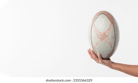 A hand firmly clasps a rugby ball, fingers gripping its textured surface with purpose. The composition leaves ample copy space, inviting the addition of text or graphics. - Powered by Shutterstock