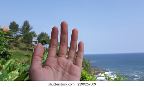 A hand with five fingers with beautiful view on the surumanis beach kebumen central java indonesia 