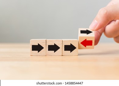 Hand flip over wooden cube block with red arrow facing the opposite direction black arrows, Unique, think different, individual and standing out from the crowd concept