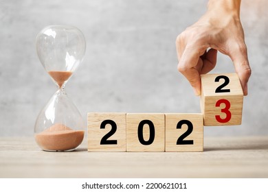 hand flipping block 2022 to 2023 text with hourglass on table. Resolution, time, plan, goal, motivation, reboot, countdown  and New Year holiday concepts
