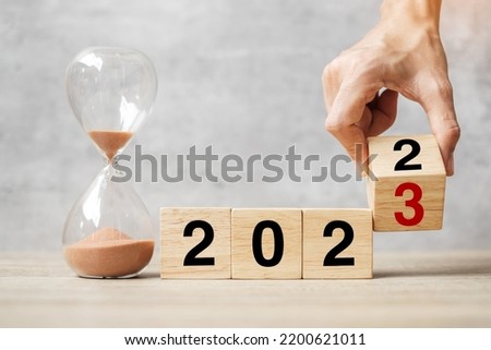 hand flipping block 2022 to 2023 text with hourglass on table. Resolution, time, plan, goal, motivation, reboot, countdown  and New Year holiday concepts