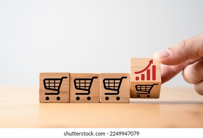 Hand flipping change between increasing graph and shopping cart trolley which print screen on wooden block cube for commerce business sales and order growth concept.