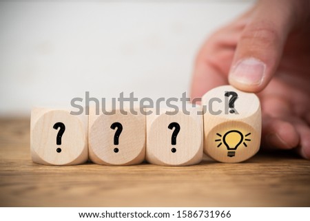 hand is flipping one of many cubes with questionmarks to find an idea symbol on wooden background