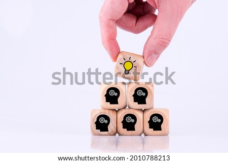 A hand flipping wooden cube with an icon of idea on top of a pyramid with brain icons