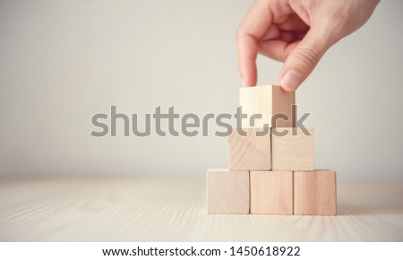 Hand flips blank wood cube block on top pyramid, for create icon symbol to success concept.