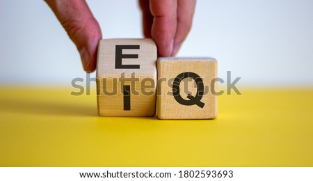 Hand flips a cube and changes the expression 'IQ' to 'EQ'. Beautiful yellow table, white background. Concept of emotional and  intelligence quotient. Copy space.