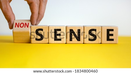 Hand flips a cube and changes the word 'nonsense' to 'sense' or vice versa. Beautiful yellow table, white background. Concept. Copy space.
