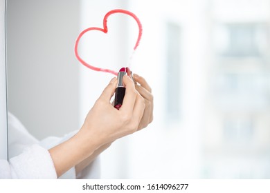 Hand flirty female in white bathrobe drawing heart and crimson lipstick mirror in the bathroom