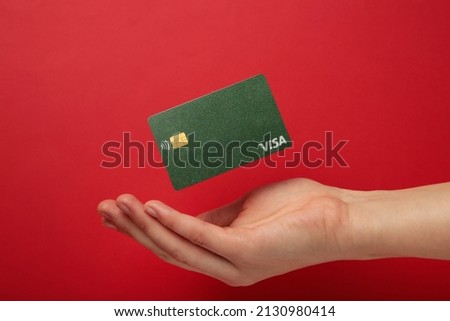 Hand with flying credit card Visa on red background. Top view