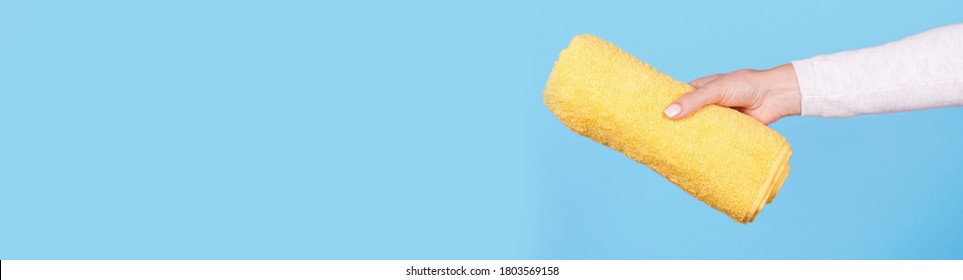 Hand With Folded Yellow Towel, Isolated On Blue Background, Copy Space Template, Banner.