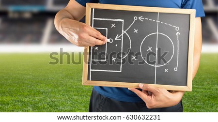 hand of a football coach drawing a tactics of soccer game with white chalk on blackboard at stadium background