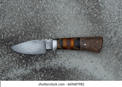 A hand forged Damascus hunter knife displayed on cement