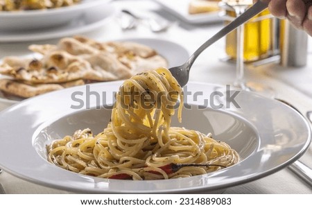 Hand with a fork spinning spaghetti aglio e olio peperoncino from a plate in a restaurant.