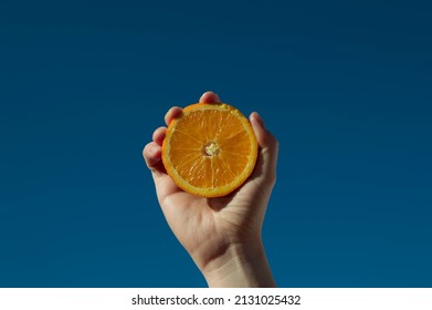 Hand With Fresh Orange Fruit On Blue Sky Background