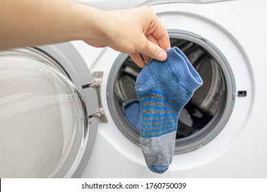 Hand vor der Waschmaschine für die Frontbeladung fand einen blauen fehlenden Sock 