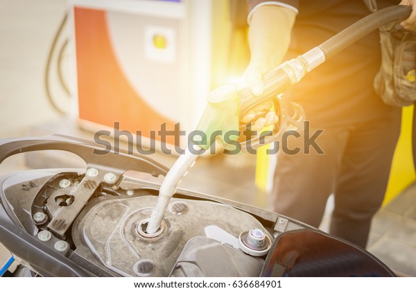 hand fuel nozzle in pouring to\
motorcycle at gas station,selective focus,vintage color\
