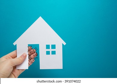 Hand with funny fingers holding white paper house figure on blue background. Real Estate Concept. Copy space top view. - Powered by Shutterstock