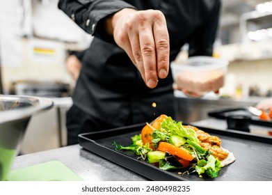 A chef’s hand garnishing a colorful salad on a plate. - Powered by Shutterstock