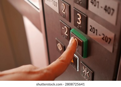 A hand gently presses the elevator button on a busy day.