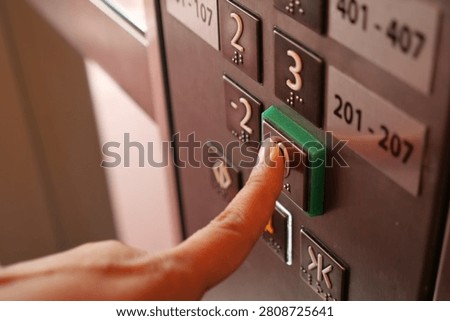 A hand gently presses the elevator button on a busy day.