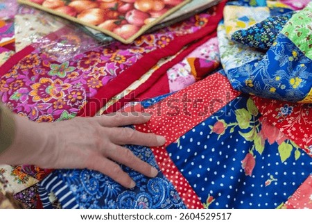 Hand gently touches bright patchwork quilt with lots of colorful floral and patterned fabrics. Buyer's Choice. Close-up.