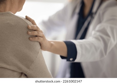 Hand of geriatrician doctor touching shoulder of elderly patient woman, giving empathy, comfort, psychological support, assistance, explaining serious diagnosis of illness. Close up cropped shot