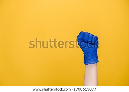 Hand gesture and coronavirus concept. Close up of female hand in medical protection blue gloves knock knock knocking on camera, isolated on yellow studio background with copy space for advertisement