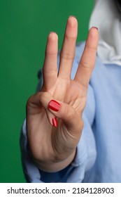 Hand gesture, female with red nail polish, on a green background. 