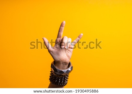 Hand gestures. Thumbs up, that's a cool gesture of the rocker. women's hand with lots of bracelets, youth fun style. bright yellow background