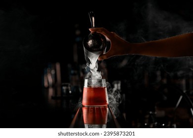 Hand of girl bartender accurate pours steaming cocktail from steel shaker into drinking glass standing on the bar counter on dark blurred background - Powered by Shutterstock