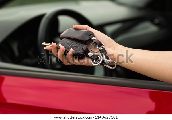 hand of a girl with a car key in hand, on a\
red car background