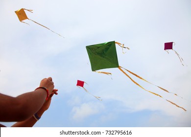 Hand of a girl raises a kite in a sky where some other kites are also flying 