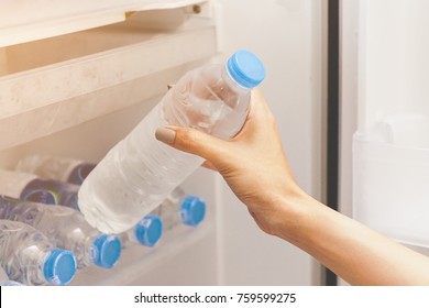 Hand of a girl taking out a water bottle or mineral water from refrigerator or a fridge on hotel or bed room or supermarket. Drinking water is beneficial to health. 