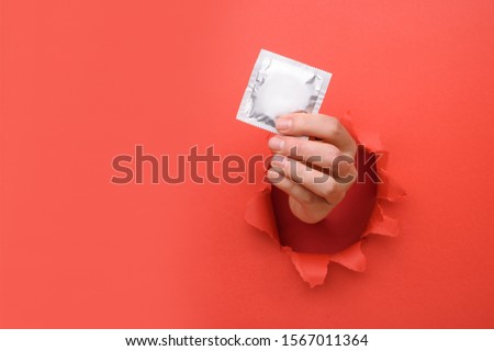 Hand give condom on torn red paper wall. Safe pleasure and protection, contraception, protection from AIDS and day to fight AIDS. Copy space aside for your advertising content