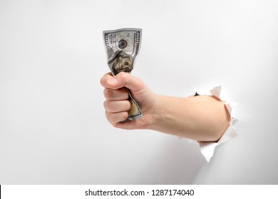 Hand give a crumpled banknote through torn white paper background. Take my money. Eagerness to buy.