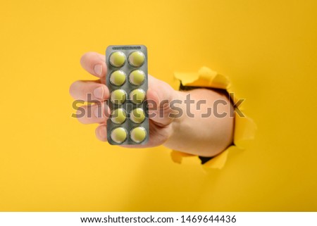 Hand giving a blister of pills through a hole torn in yellow paper wall. Health care and pharmaceutical breakthrough.