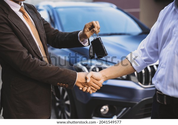 Hand giving a car key with handshake for car\
transaction deal concept
