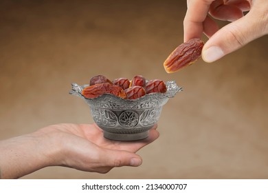 hand giving date fruit. Vintage metal bowl full of pitted date fruits on wooden table.  Traditional iftar food. Symbolizing Ramadan. - Shutterstock ID 2134000707